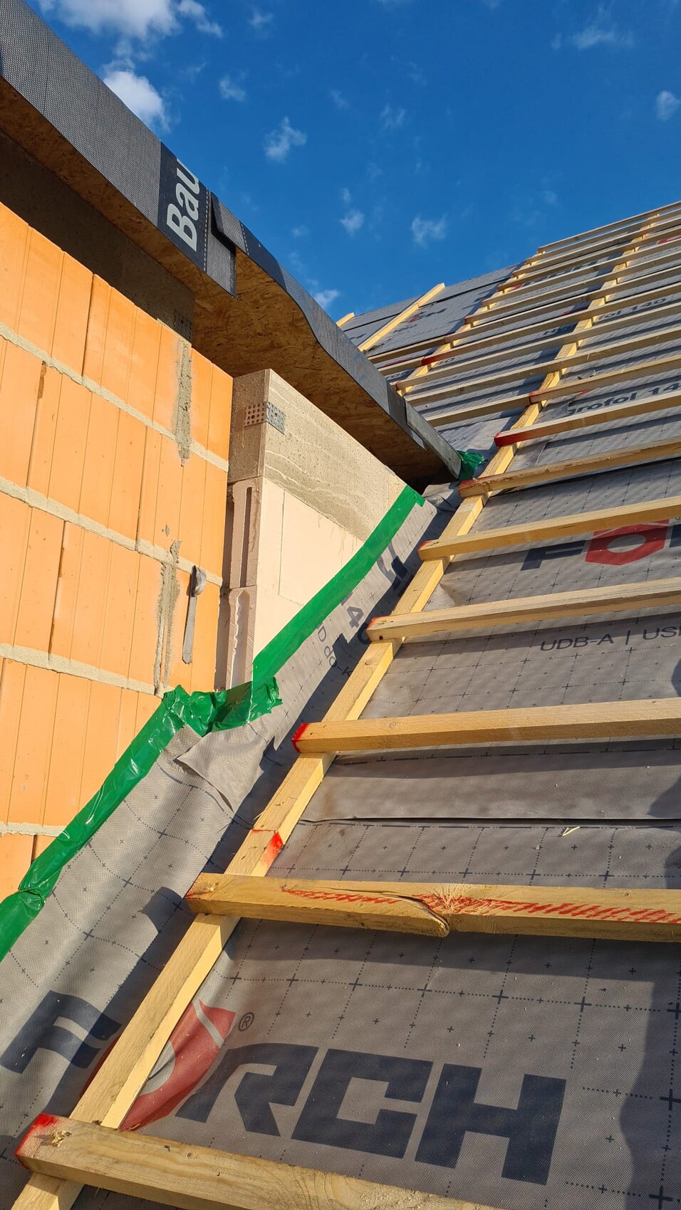 Bau-Dachkonstruktion mit Dachlatten, Unterlage, grünem Band, blauer Himmel