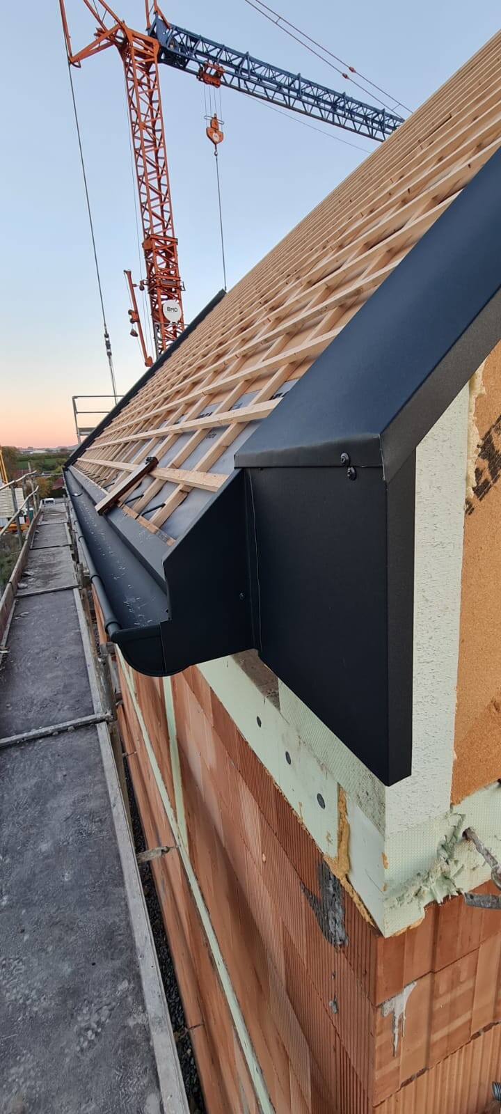 Baukran über Dachkonstruktion aus Holzlatten; Baugerüst an der Fassade.