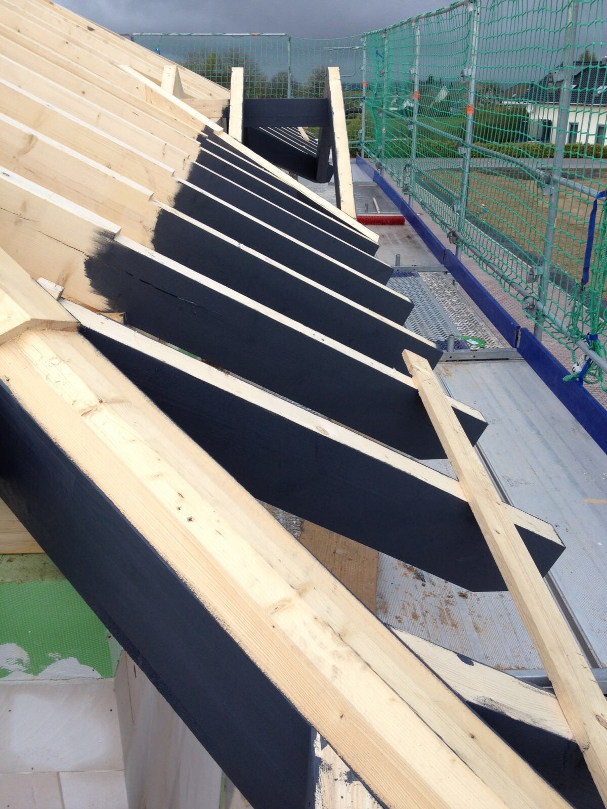 Dachkonstruktion im Bau: Holzbalken, schwarze Dichtungsbahn, grüne Baugerüstnetze.