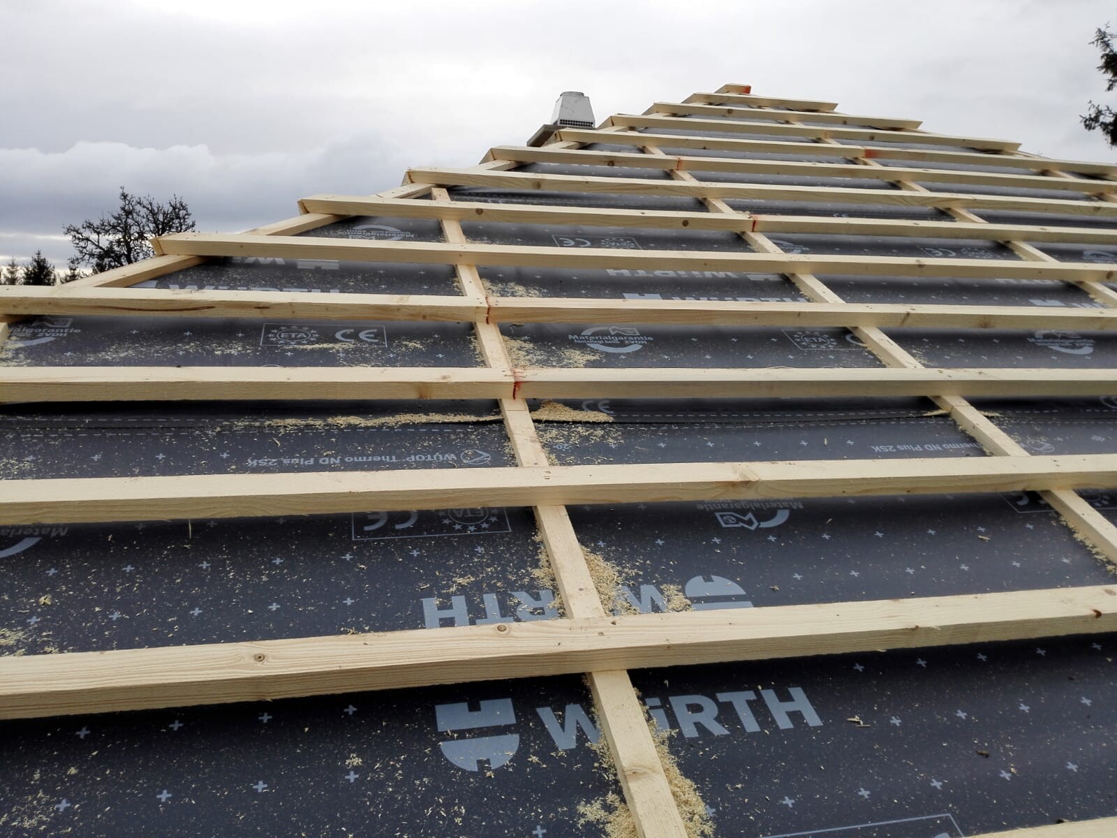 Dachkonstruktion mit Holzlattenrahmen über schwarzer Dachbahn, wolkiger Himmel