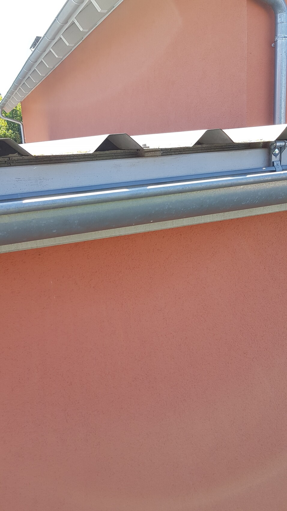 Rosa verputzte Hauswand mit Dachrinne, Fallrohr und Dachkante