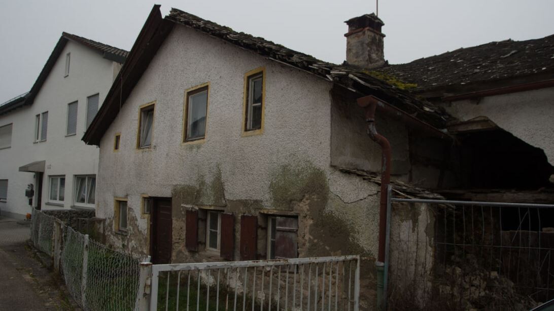 Angegriffenes Haus mit Dachschaden, bröckelnder Fassade und verrosteter Regenrinne von außen