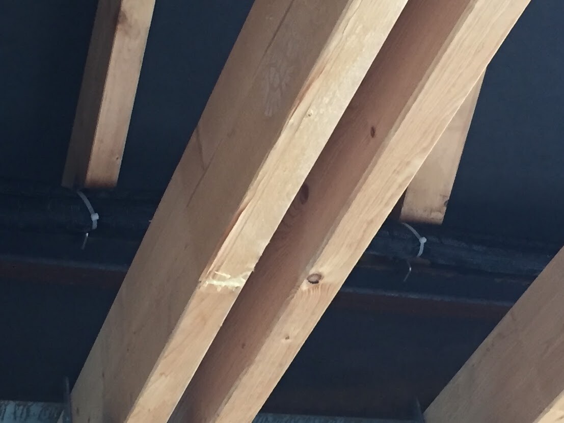 Dachstuhl mit schrägen Holzbalken im Innenraum, dunkler Hintergrund, sichtbare Kabel