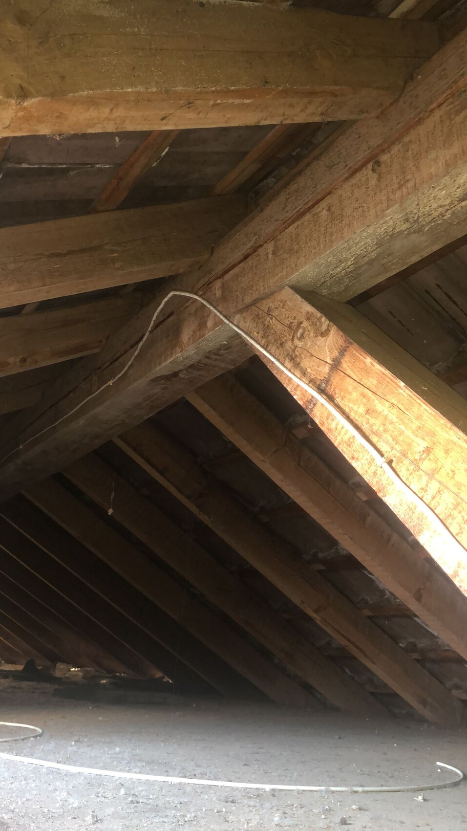 Dachstuhl aus Holzbalken im Dachboden mit sichtbaren Kabeln und Staub am Boden