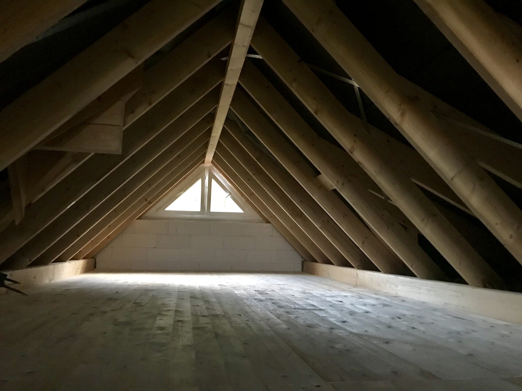Dachboden mit sichtbaren Holz-Dachstuhlträgern und kleinem Giebel-Fenster