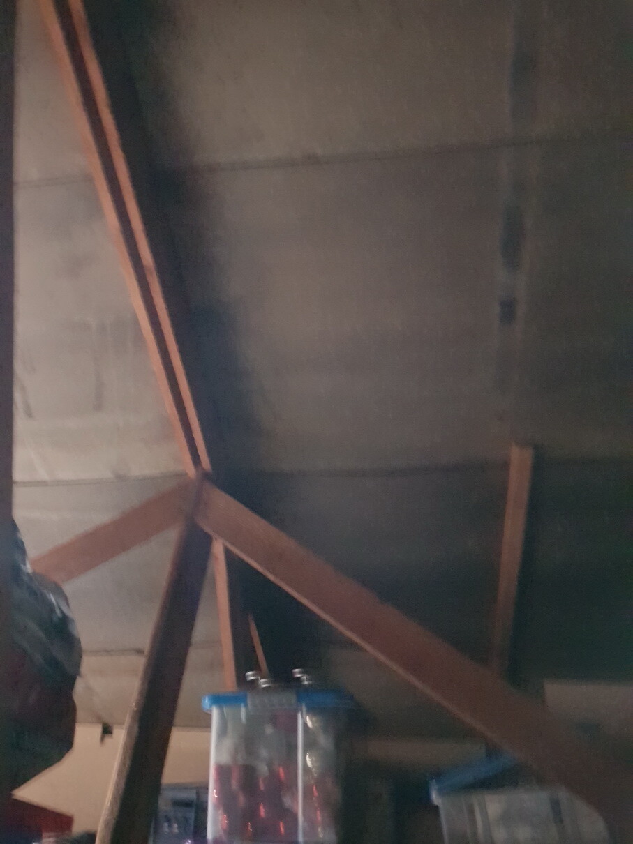 Ein Dachstuhl im Dachgeschoss mit Holzbalken und Sparren, dunkler Bereich der Baustelle