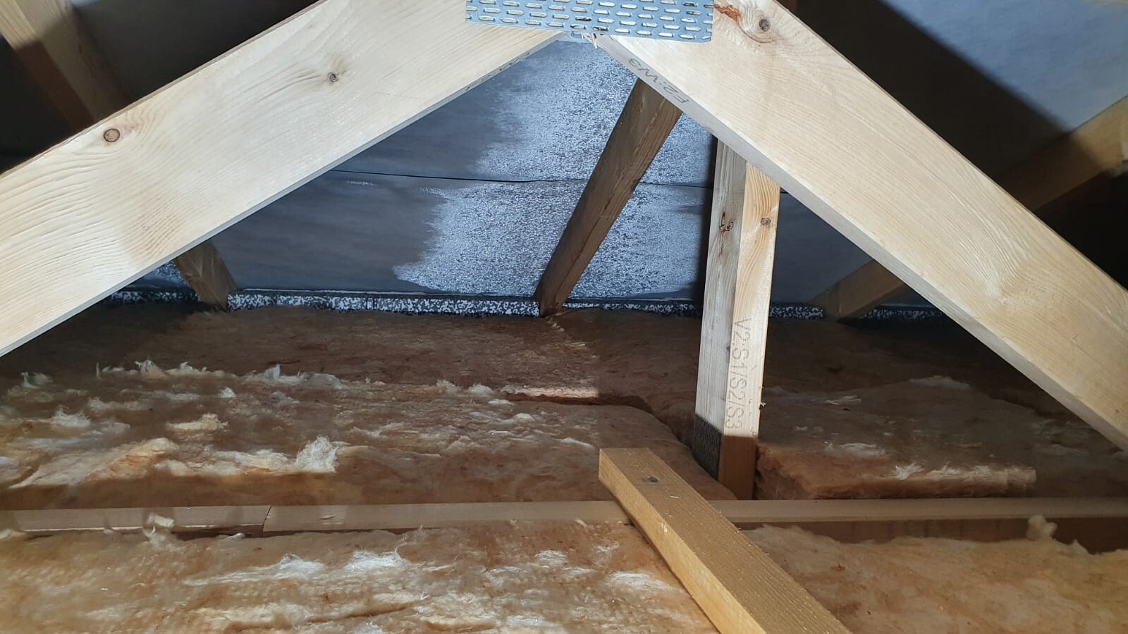 Dachboden mit sichtbarem Holzdachstuhl, Stützbalken und Dämmstoff auf dem Boden.
