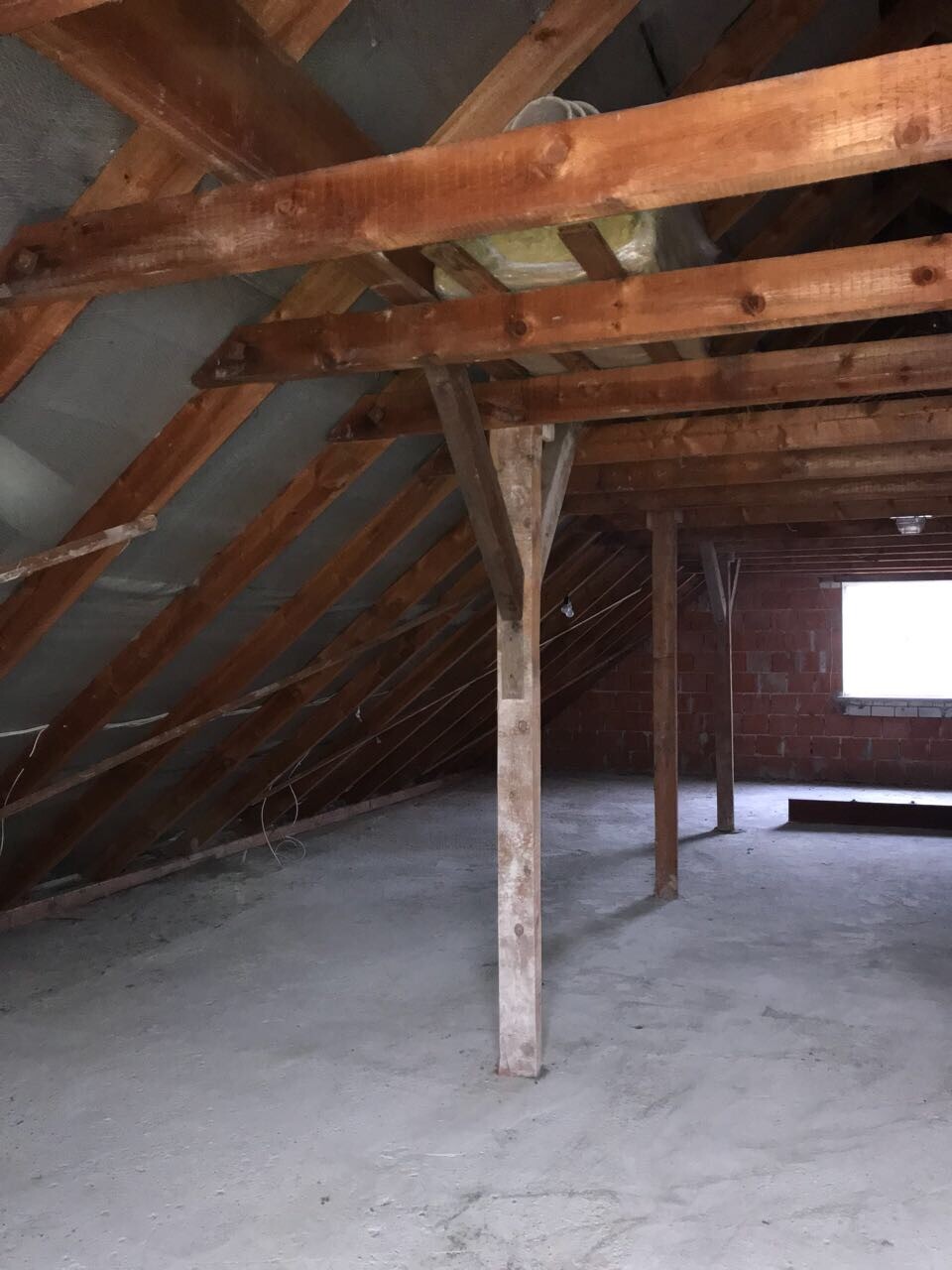 Dachboden mit sichtbaren Holzbalken, Sparrenwerk und unfertigem Boden.