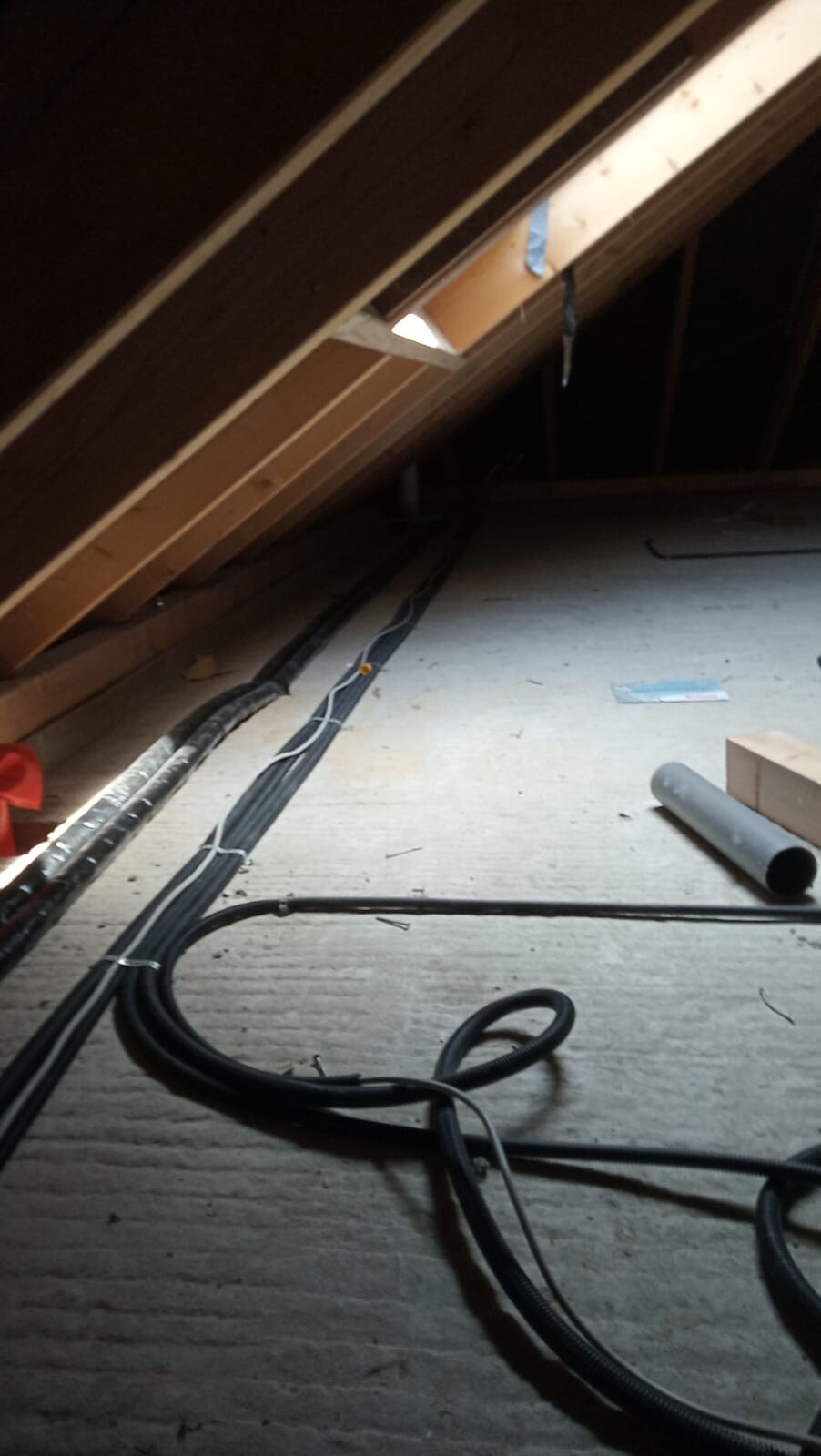Dachboden mit sichtbarem Dachstuhl, Kabeln und Baumaterialien auf einer Baustelle