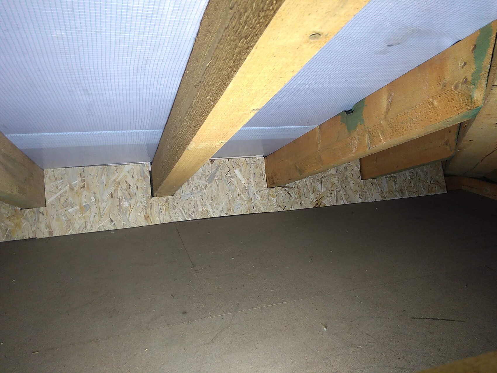 Dachboden mit sichtbaren Holzbalken, blauen Dämmplatten und OSB-Verkleidung.