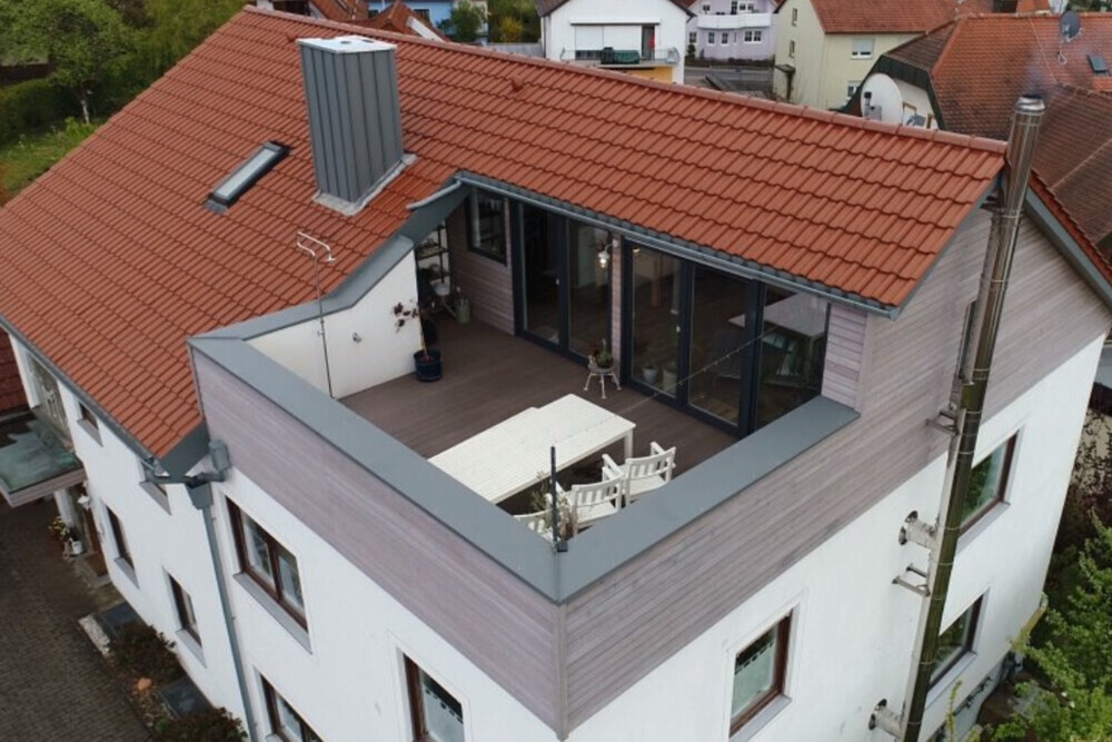 Dachterrasse eines Wohnhauses mit Outdoor-Möbeln und Glasfronten.