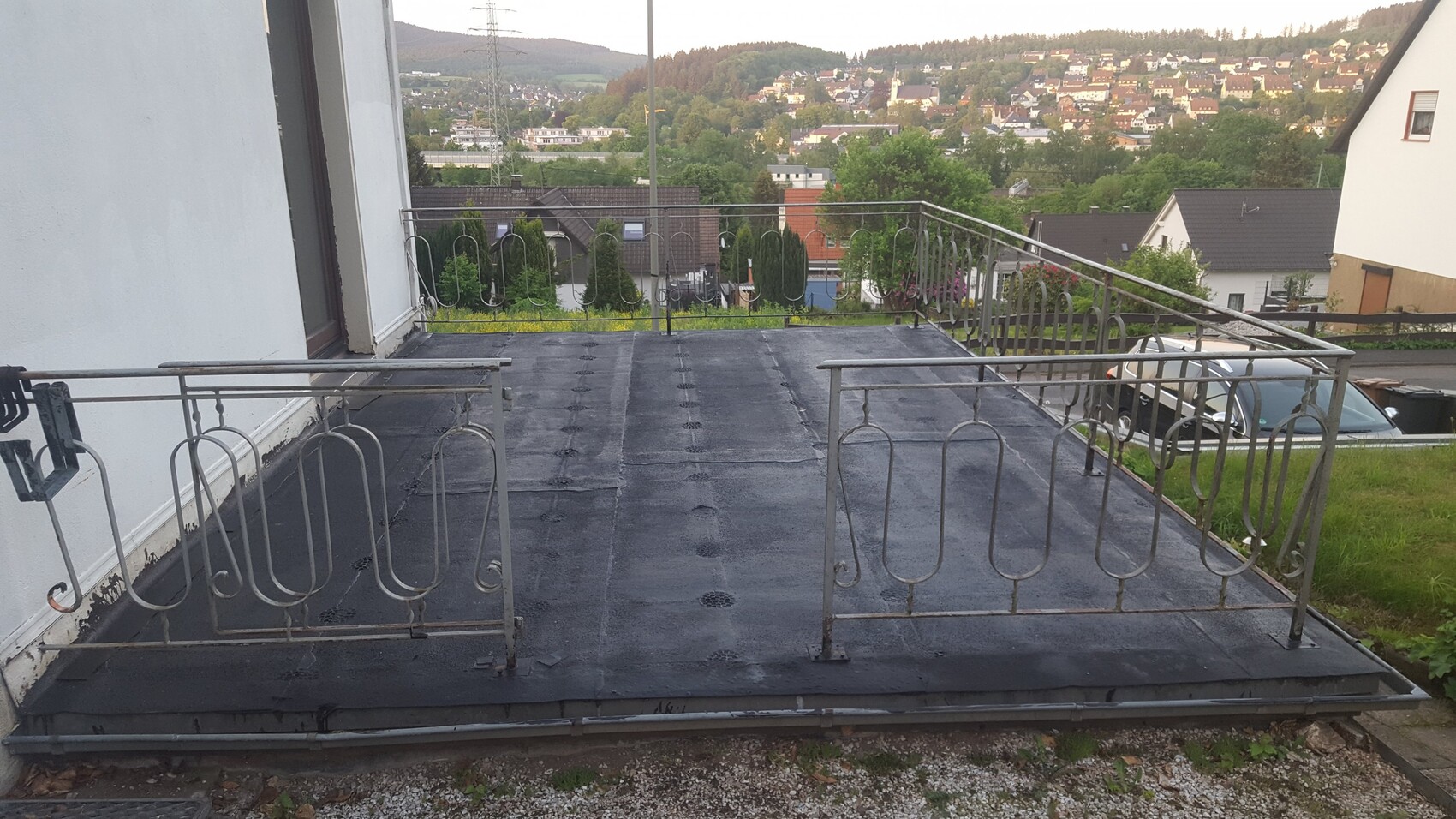 Dachterrasse mit schwarzer Abdichtung und schmiedeeisernem Geländer; Blick auf Häuser am Hang.