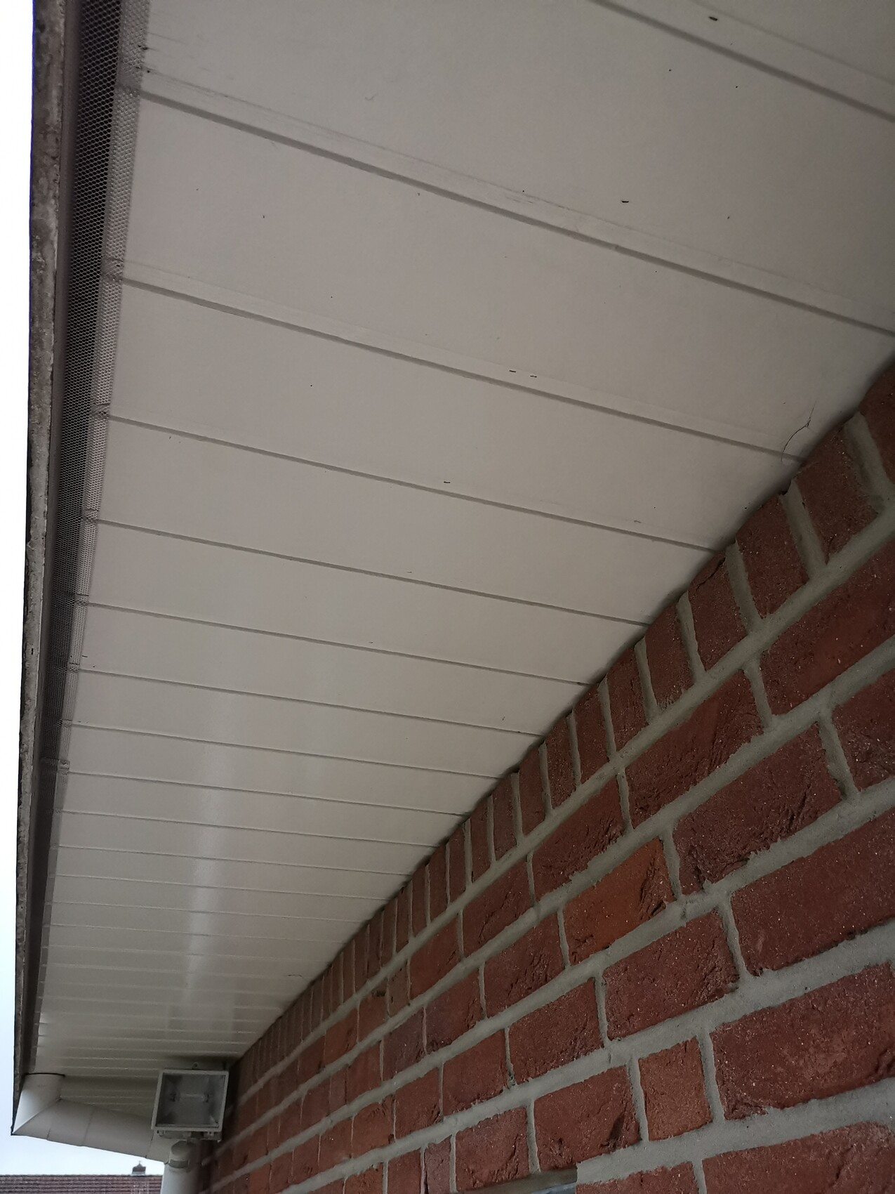 Außenansicht eines Gebäudes mit weißer Dachverkleidung und rotem Backstein an der Fassade