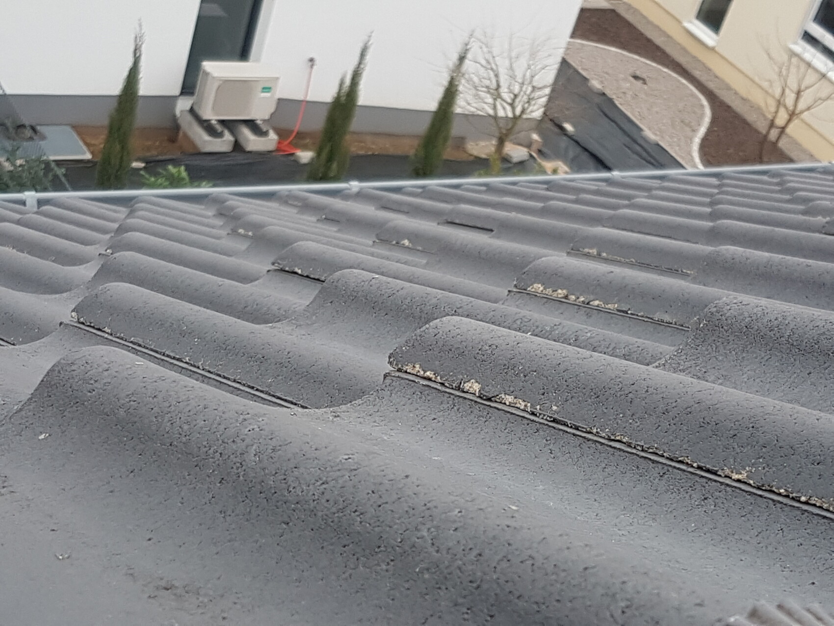 Graues Dach mit wellenförmigen Ziegeln, Außenansicht eines Wohnhauses mit Klimagerät.