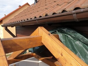 Holzgeländer und Holzbalken vor rotem Dachziegel-Dach, grüne Abdeckung sichtbar