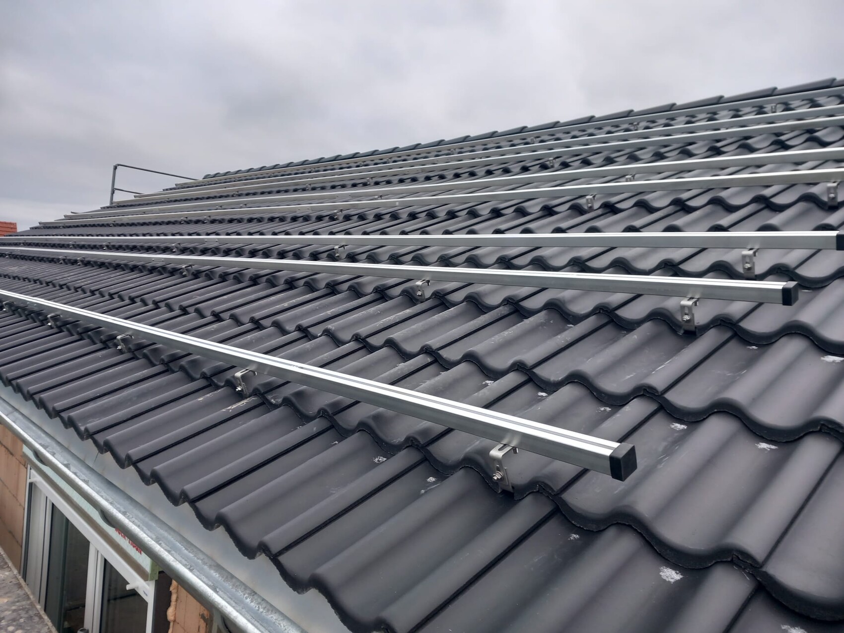 Dach mit grauen, gewellten Ziegeln und silbernen Trägern für Solarmodule