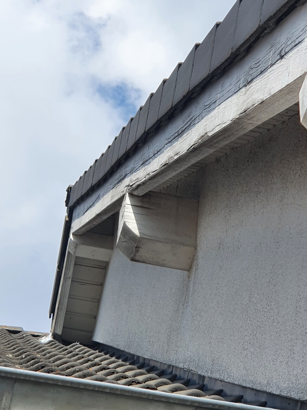 Weiße Fassade mit Dachüberstand, grauen Dachziegeln und sichtbaren Holzelementen.