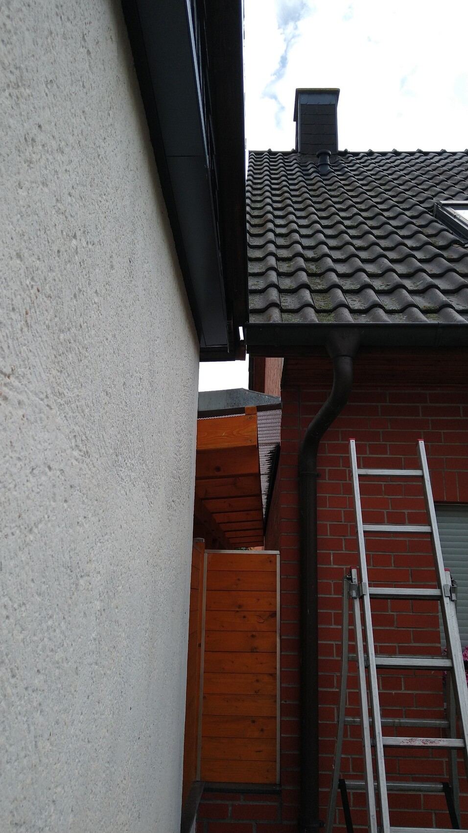 Außenansicht eines Hauses: Dachziegel, dunkle Regenrinne, rote Ziegelwand, Leiter daneben