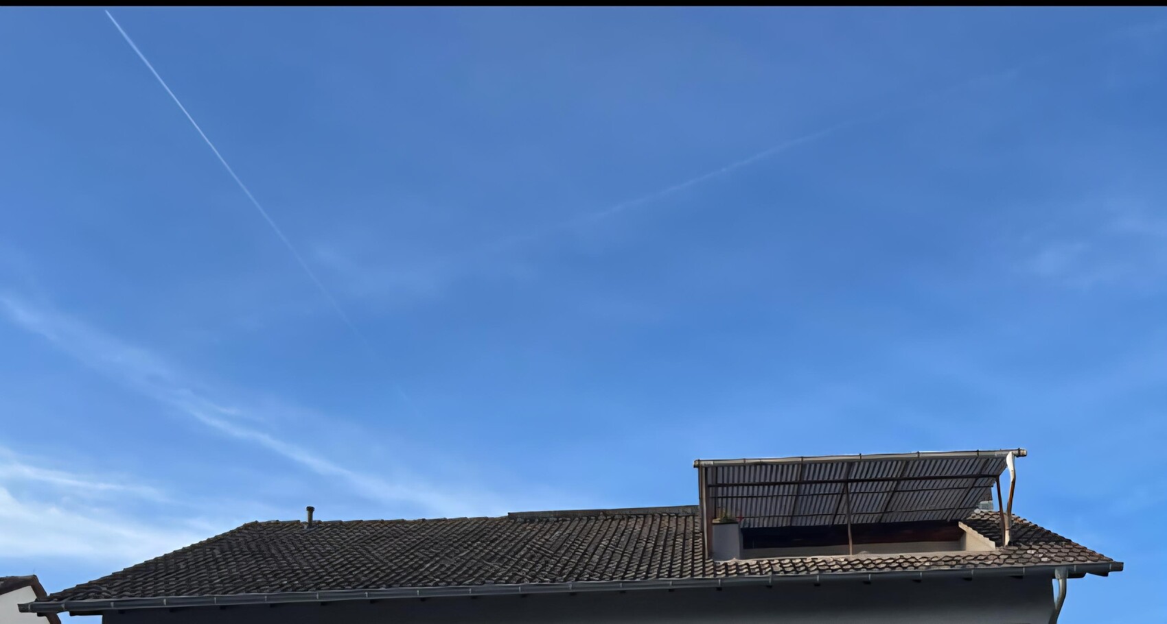 Dach mit Ziegeln und eine kleine Dachterrasse gegen blauen Himmel.