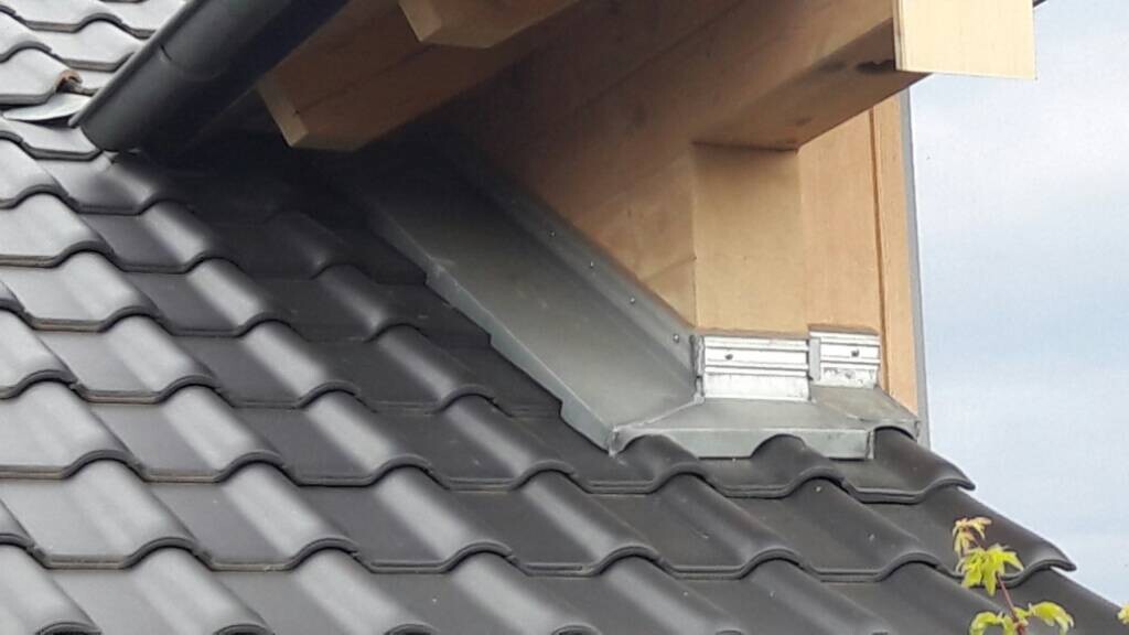 Dach mit dunkelgrauen, gewölbten Ziegeln und Metallabdeckung an der Holzwand.