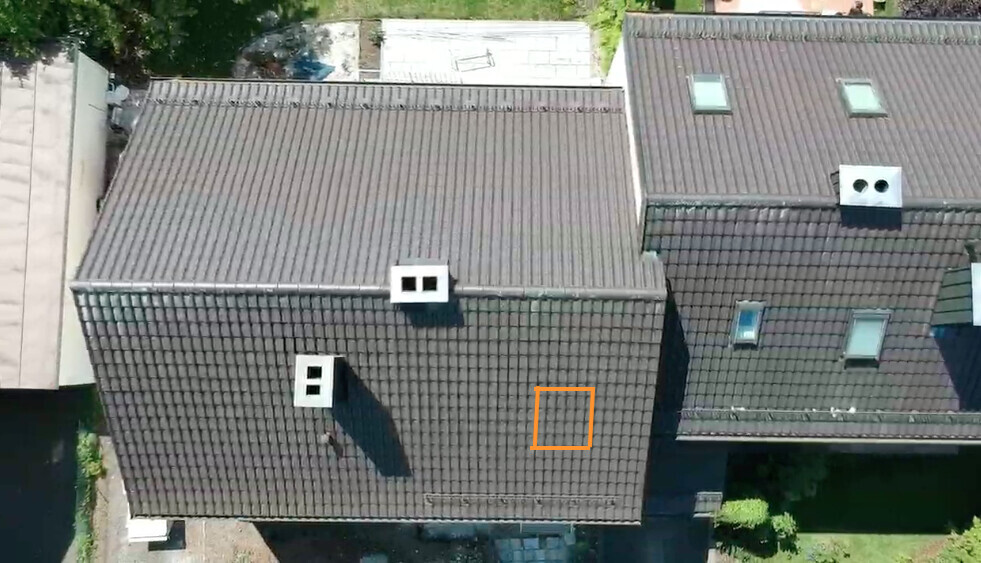 Vogelperspektive: Mehrere dunkle Ziegeldächer; orangenes Quadrat markiert eine Stelle.