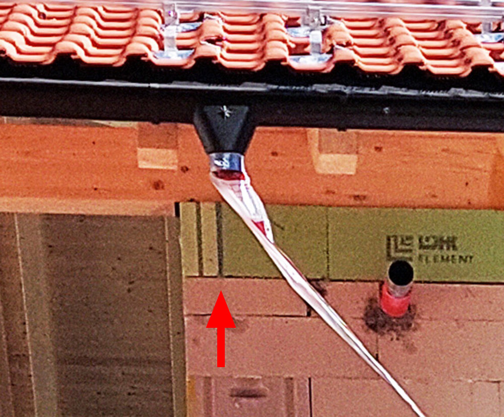 Dach mit roten Ziegeln; von der Kante hängt ein weißes Band herab, roter Pfeil markiert.