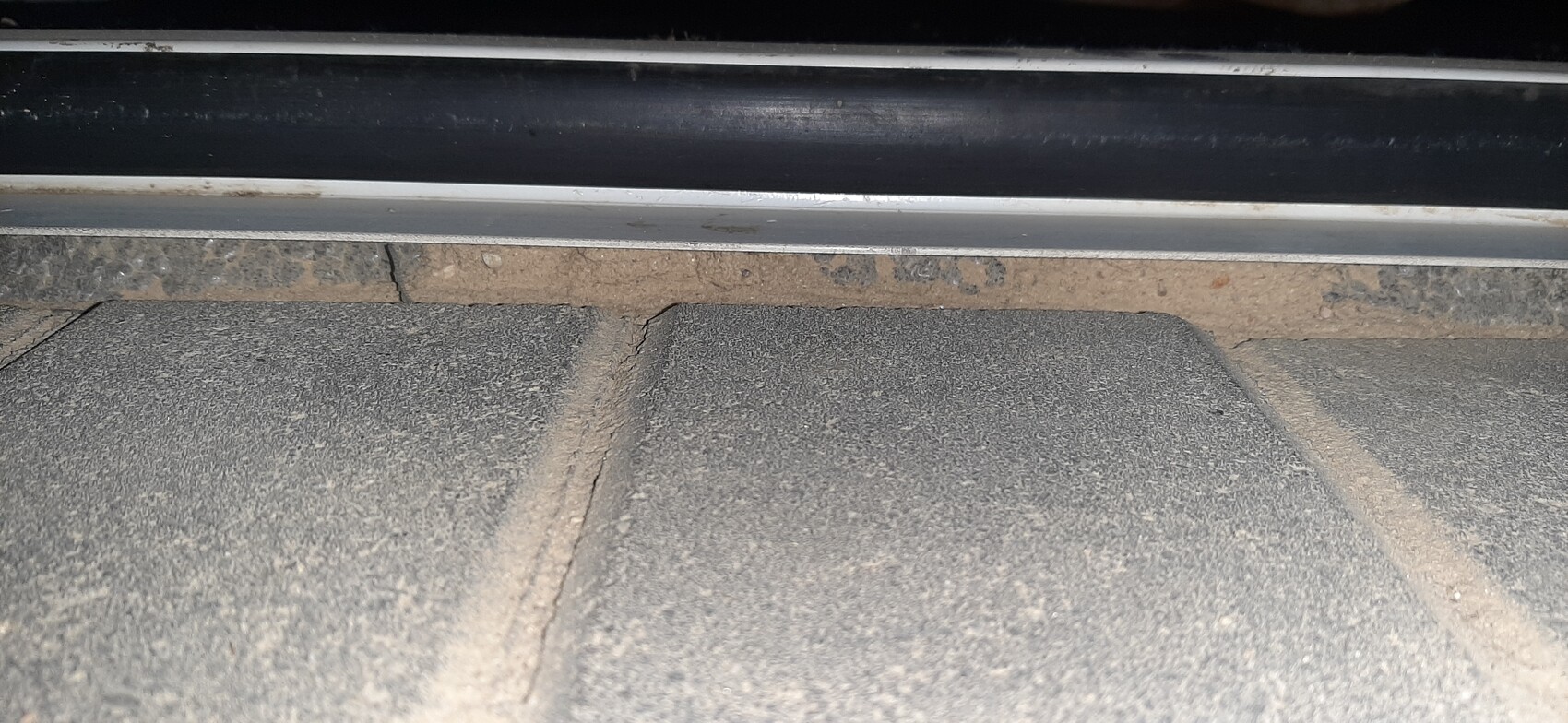 Unterseite eines schwarzen Wagens über staubigem Asphalt mit Risskante am Boden.