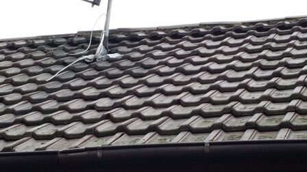 Dach mit dunkelbraunen Dachziegeln und Satellitenschüssel am First