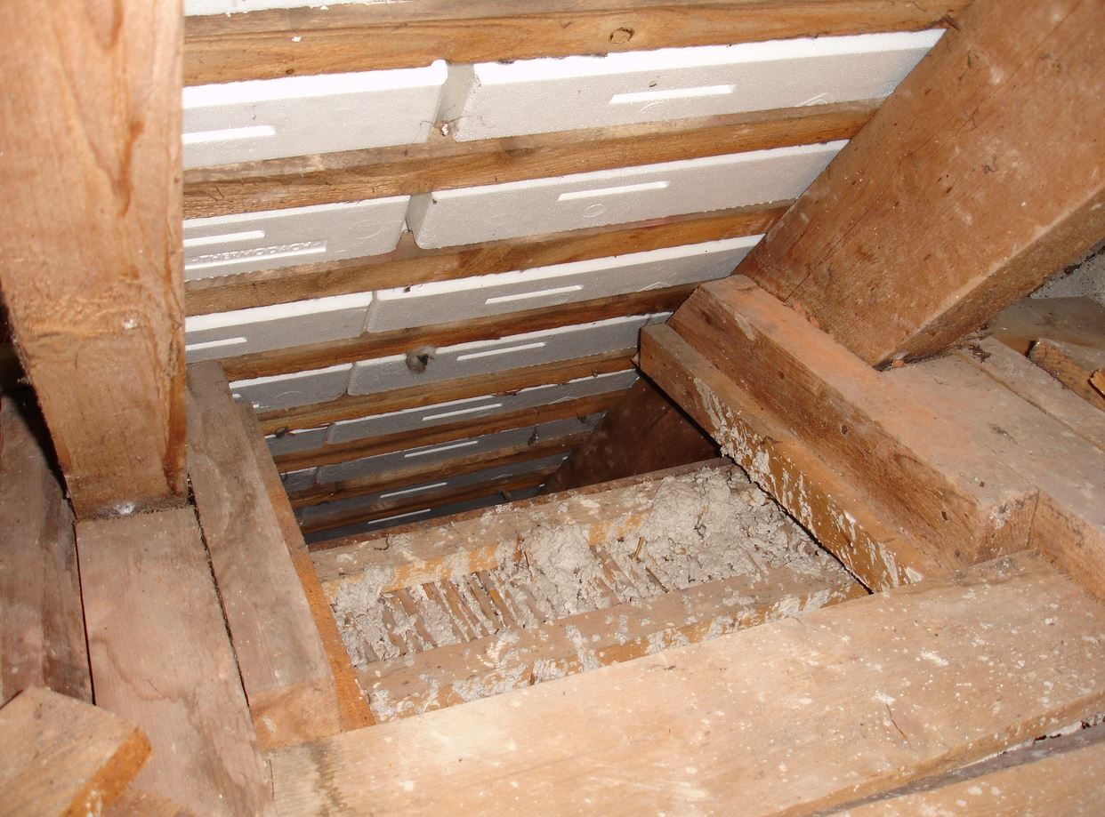 Dachboden mit Holzbalken, Dämmplatten und Staub zwischen Sparren