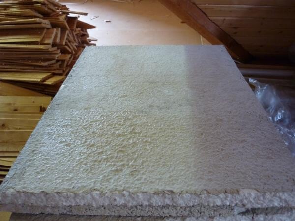 Große weiße Isolationsplatte aus Schaumstoff vor Holzwand, links Holzstapel.