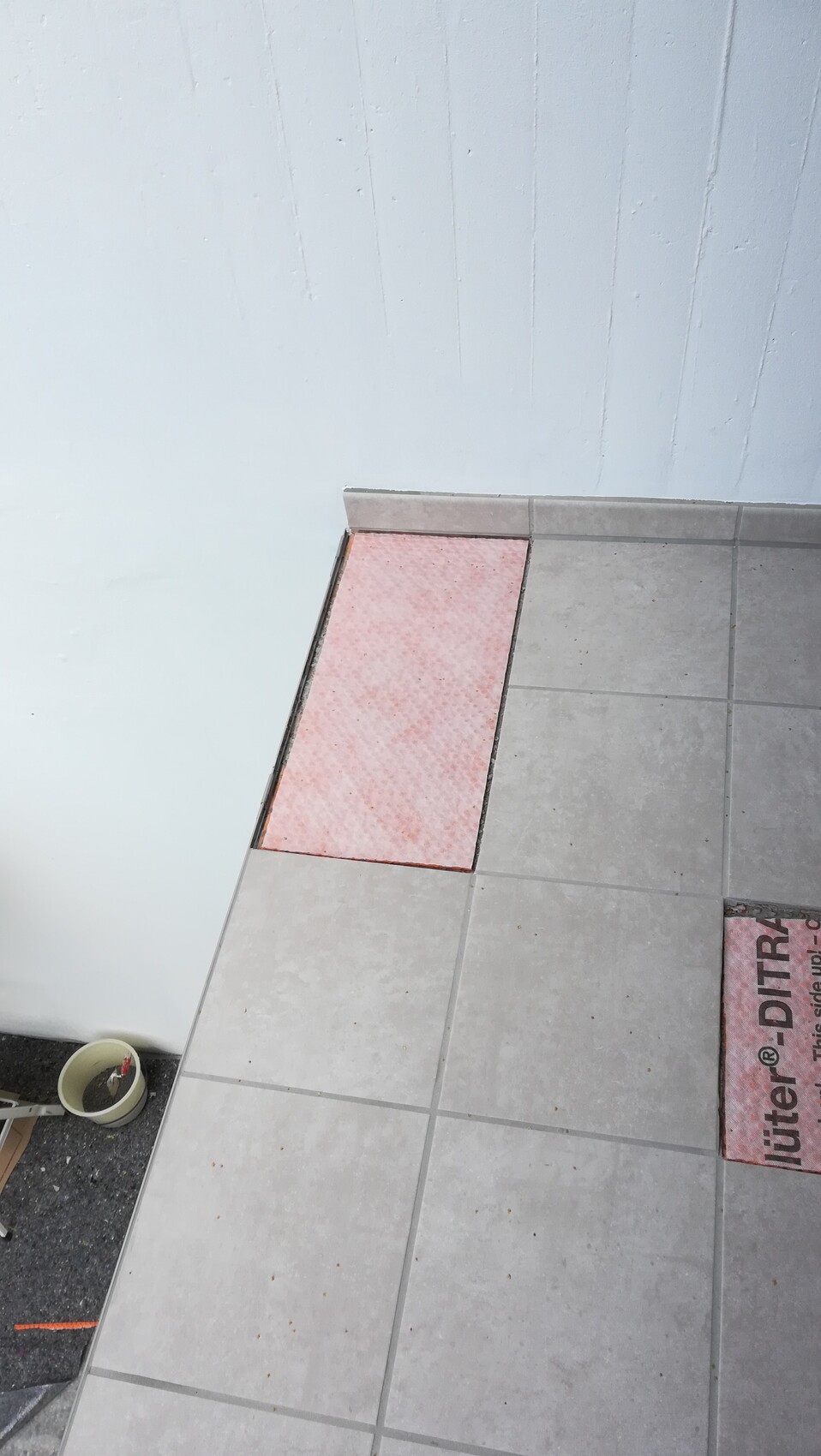 Fliesenboden mit freigelegter rosa Dämmplatte zwischen Fliesen neben einer blauen Wand.