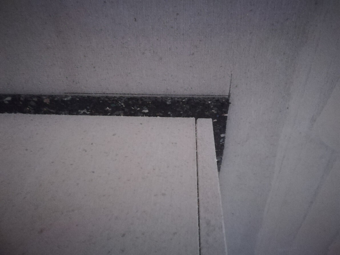 Weiße Styroporplatten stapeln sich in einer Ecke vor grauer Wand; dunkler, körniger Streifen.