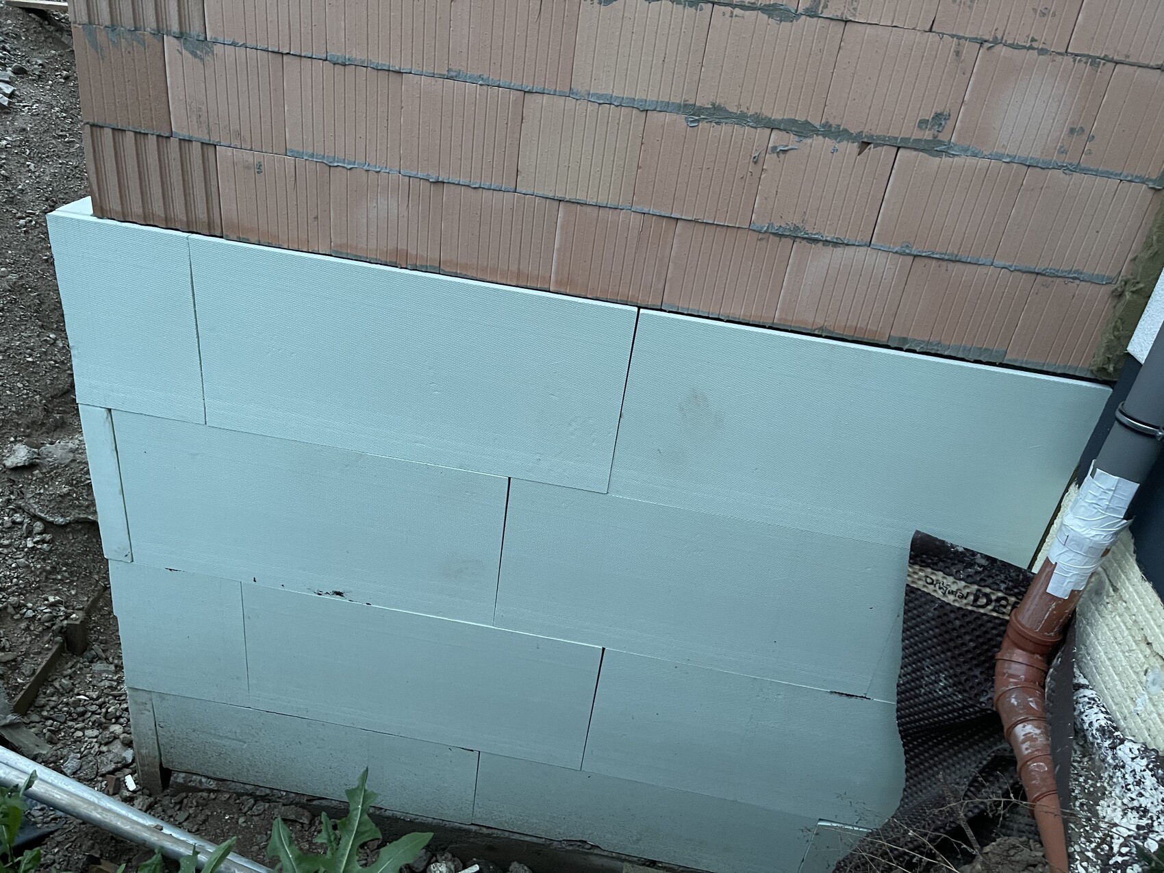 Außenwand mit hellblauen Dämmplatten (Styropor) unter Backsteinwand; Rohrleitung am Rand.