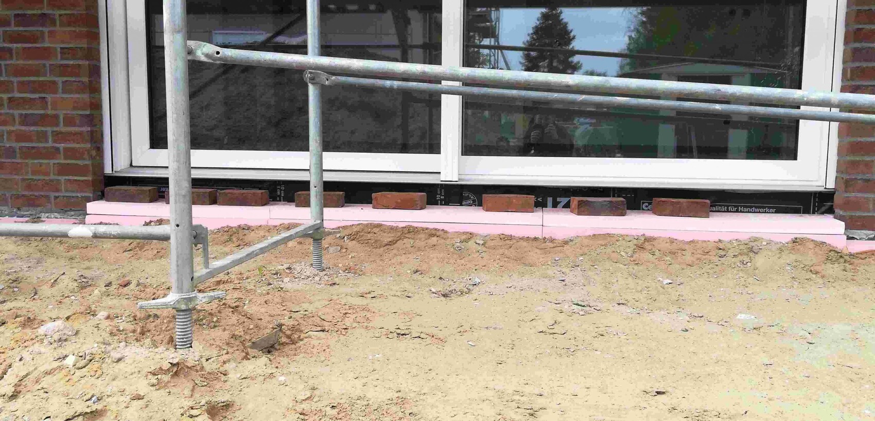 Baustelle am Haus: Stützen vor Fenster und rosa Dämmplatten an der Außenwand
