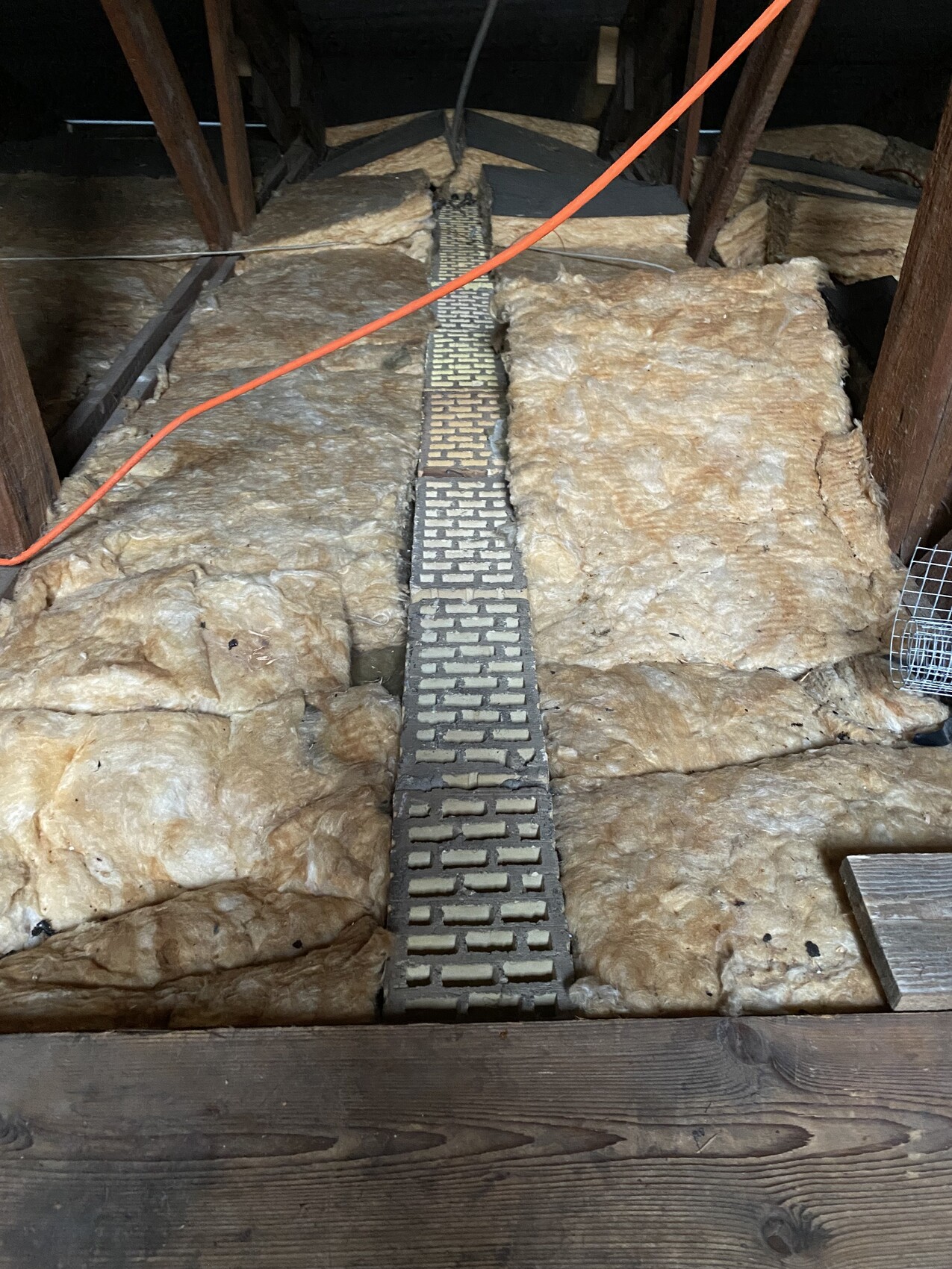 Dachboden mit Dämmung, Holzbalken, orange Kabel und schmalem Metallgitterweg in der Zwischendecke