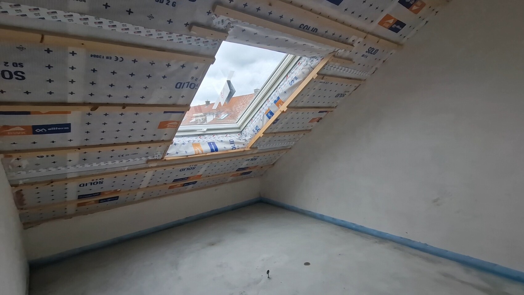 Dachgeschossraum mit Dachfenster, sichtbarer Dämmung und unfertigen Wänden.