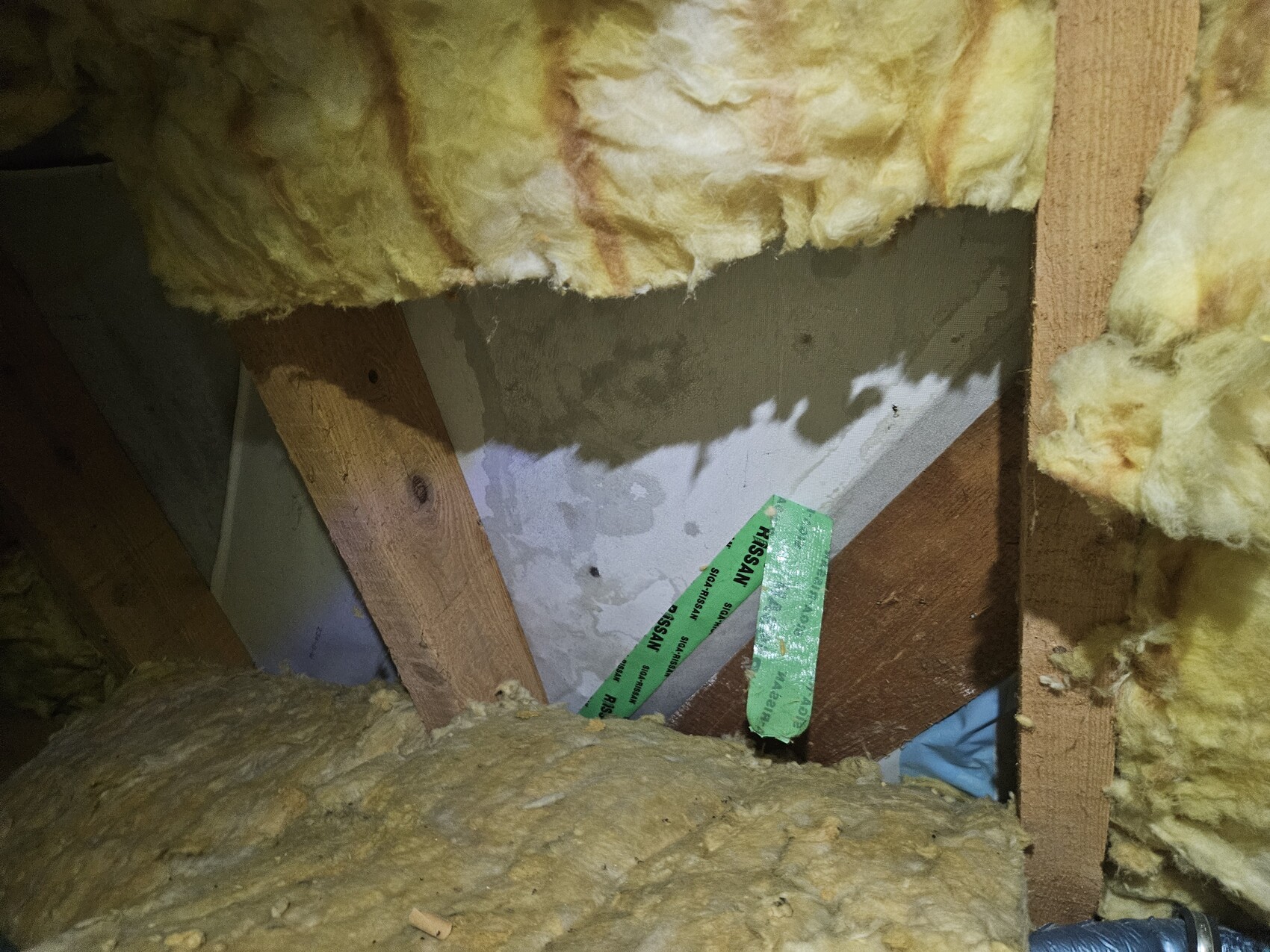 Dachboden: gelbe Isolierung zwischen Holzbalken, grünem Klebeband sichtbar.