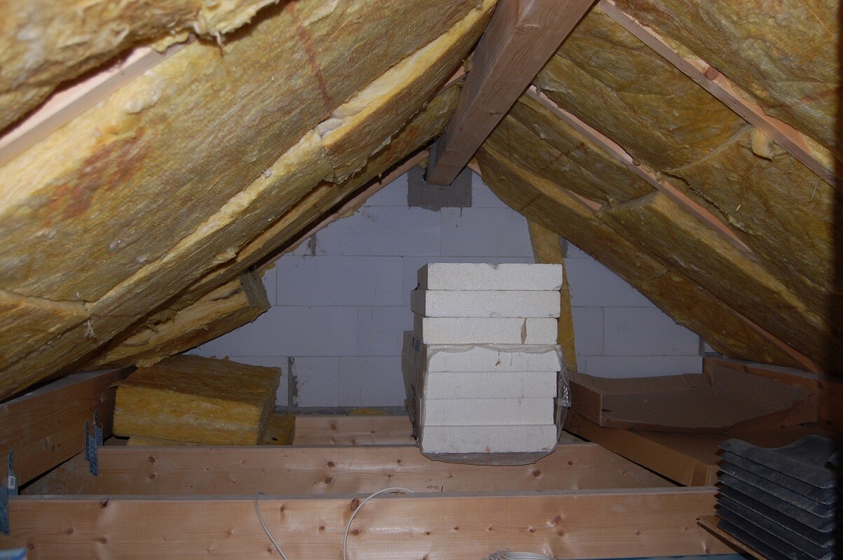 Dachboden mit Dämmung in Dachschrägen, Holzbalken und Baumaterialien.
