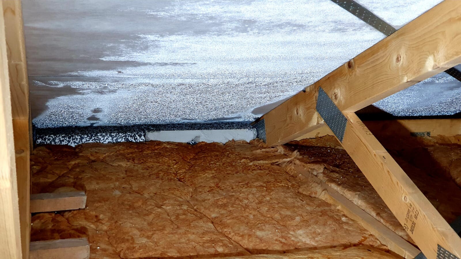 Dachboden mit Holzbalken, orange Mineralwolle-Dämmung und reflektierender Dachfolie.
