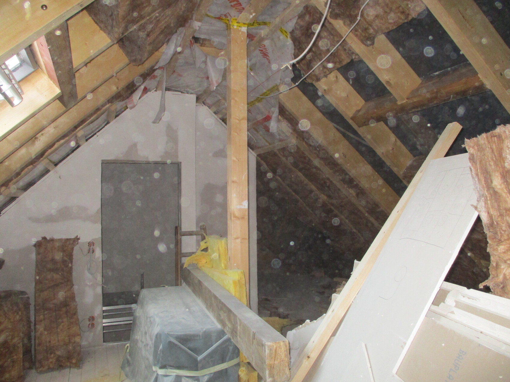 Dachboden mit Holzbalken, Dämmung, Bauplatten und Werkzeugresten; staubig.