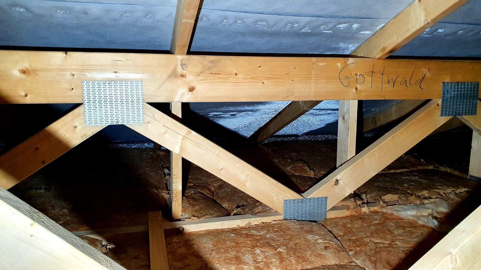 Holz-Dachstuhl mit Sparren, Metallplatten an Verbindungen, Dämmmaterial sichtbar; Schriftzug Gottwald