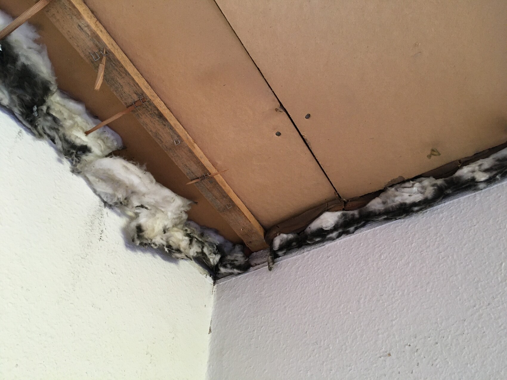 Decke mit braunen Holzplatten, lose Dämmwolle und Spalt zwischen Platte und Wand.