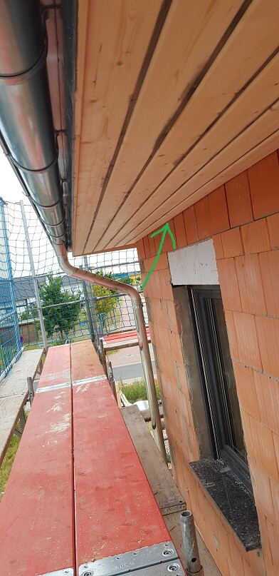 Baustelle an Ziegelwand mit Dachrinne, Fenster und Gerüst; grüne Pfeilmarkierung zeigt Fassade.