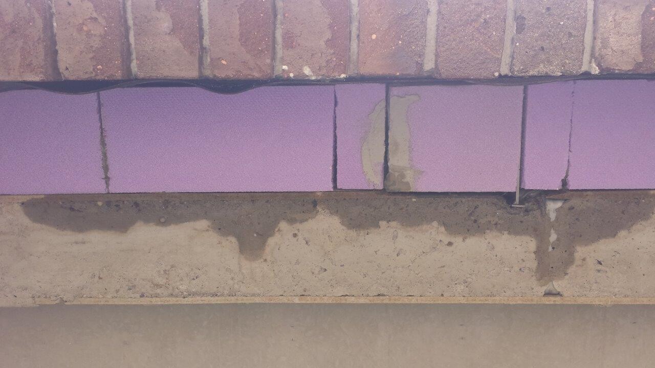 Außenwand mit violetten Dämmplatten zwischen Ziegeln, darunter Betonboden und Erde.