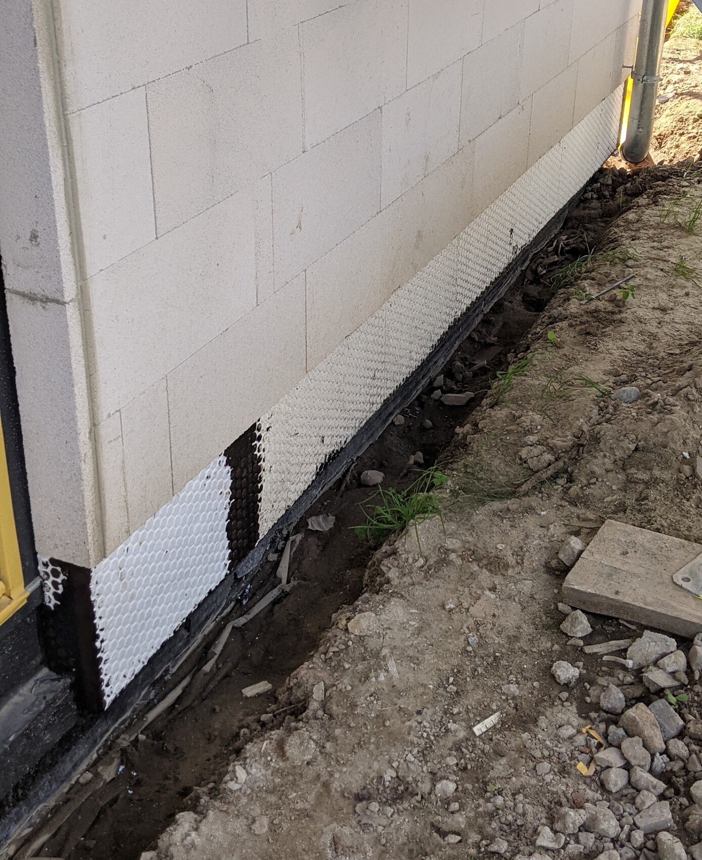 Außenwand aus weißen Porenbetonsteinen; Dichtung/Drainage-Matte am Sockel, Erde und Kies daneben.