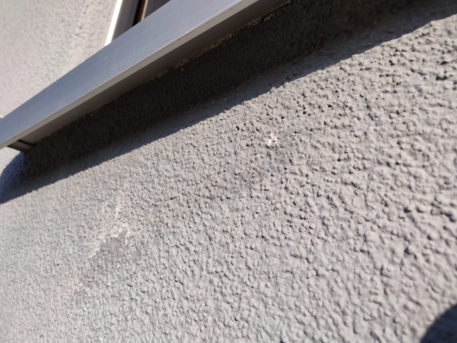 Nahaufnahme einer rauen verputzten Außenwand mit einem Metallfensterrahmen