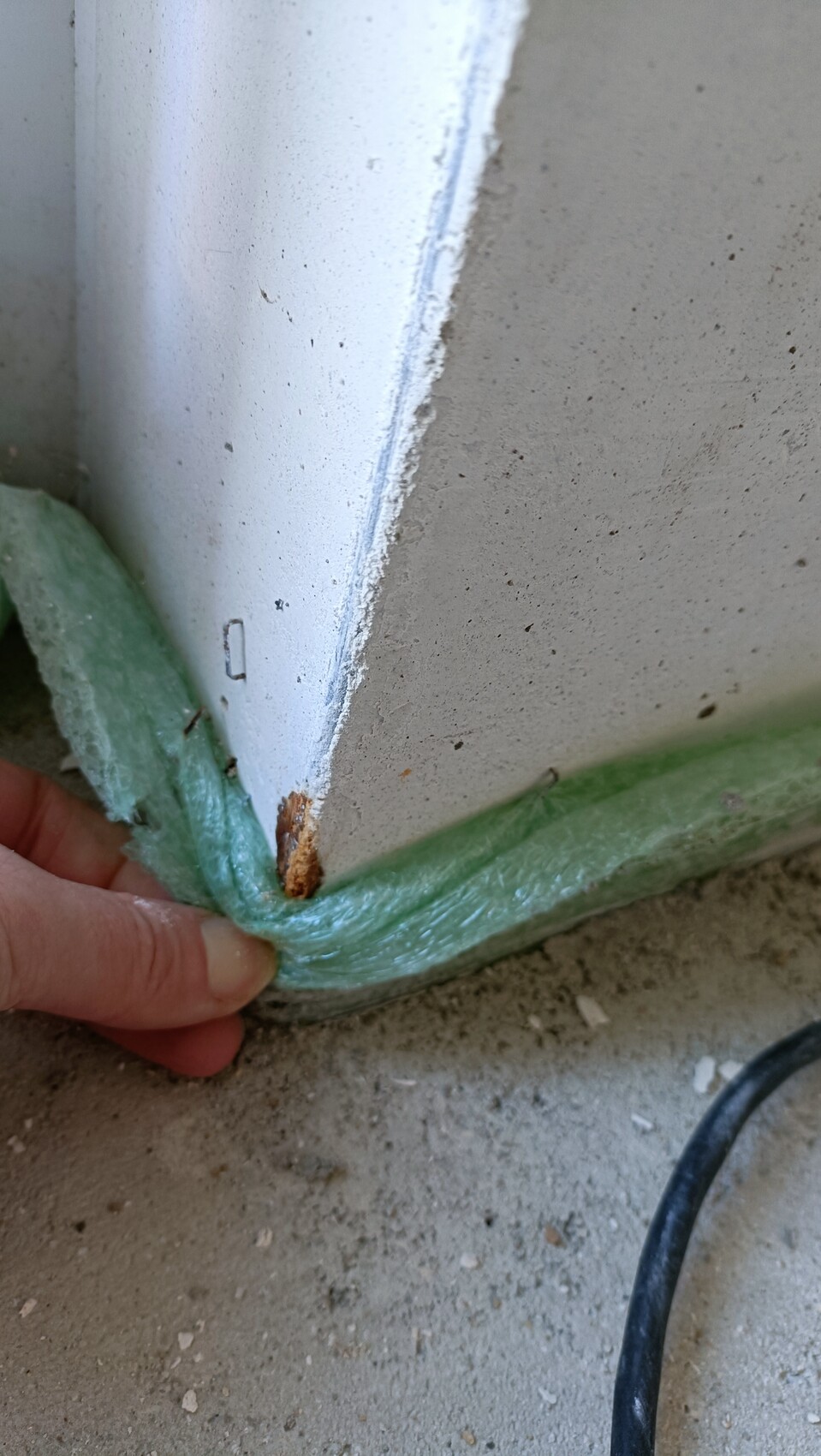 Person befestigt grünes Schaum-Dichtungsband am Türrahmen einer Betonwand; Kabel liegt am Boden.