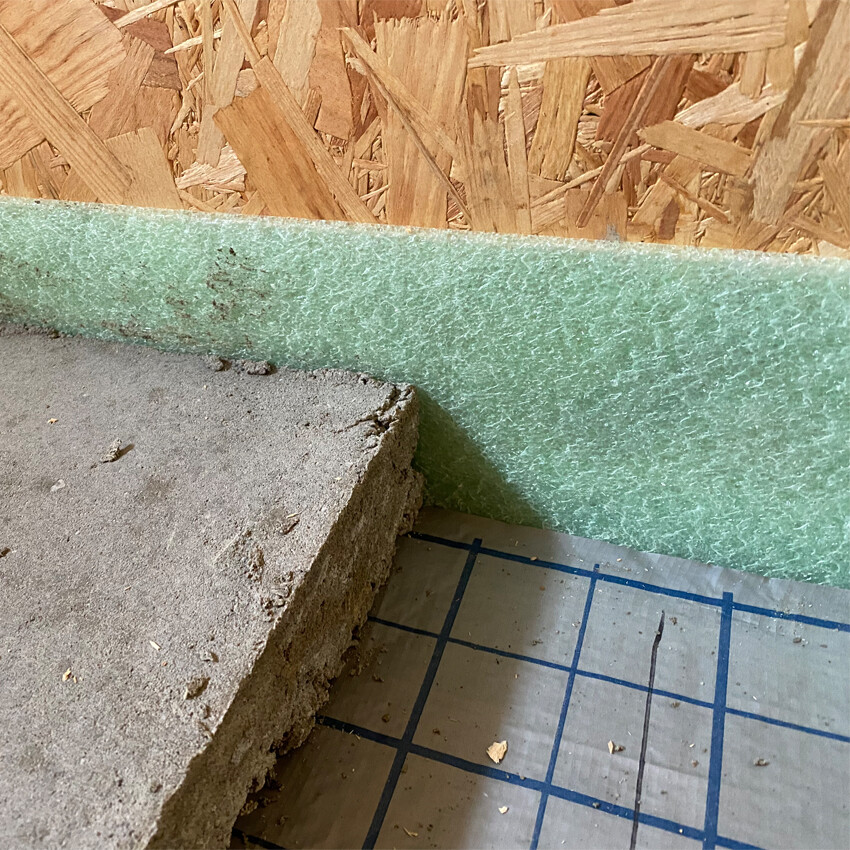 Baustelle: grüne Dämmplatten an OSB-Wand, roher Betonboden mit blauer Rastermarkierung.