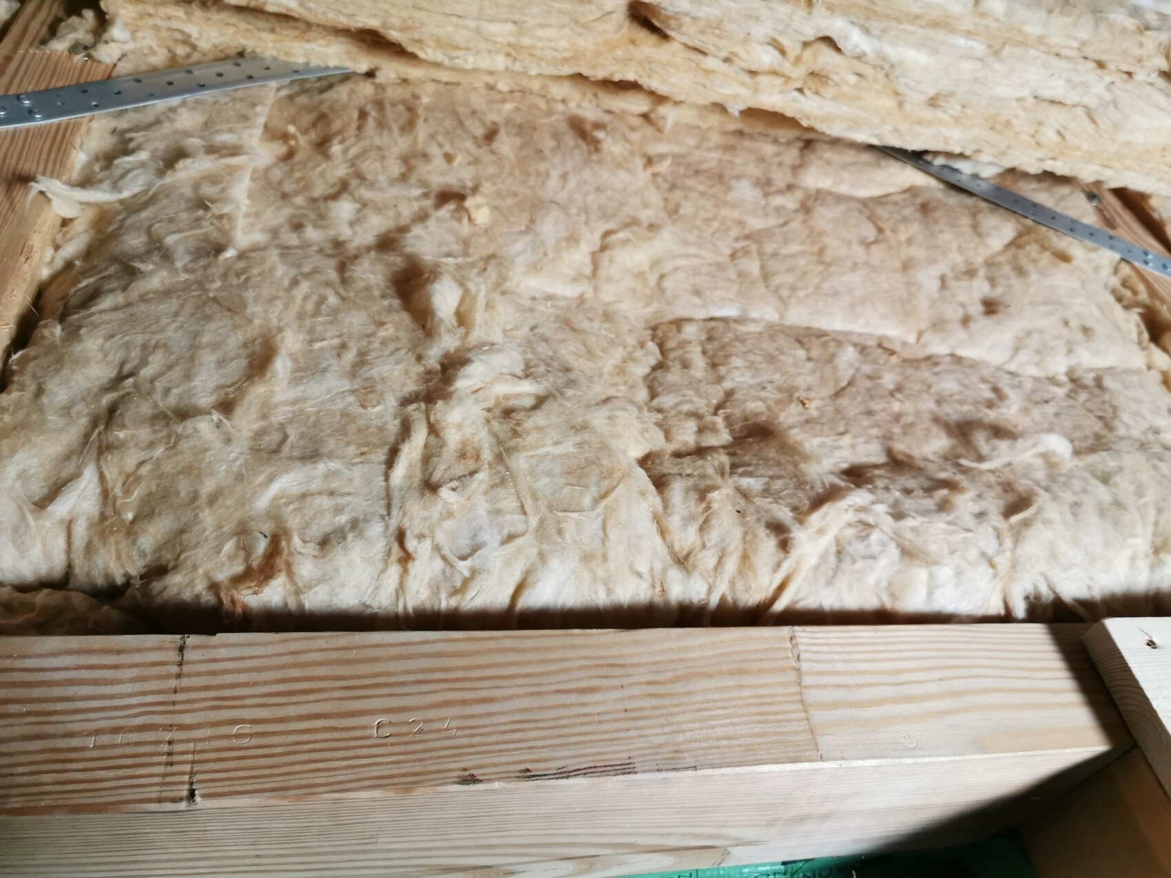 Isolationsmaterial aus Mineralwolle zwischen Holzbalken; Metalllineal liegt oben.