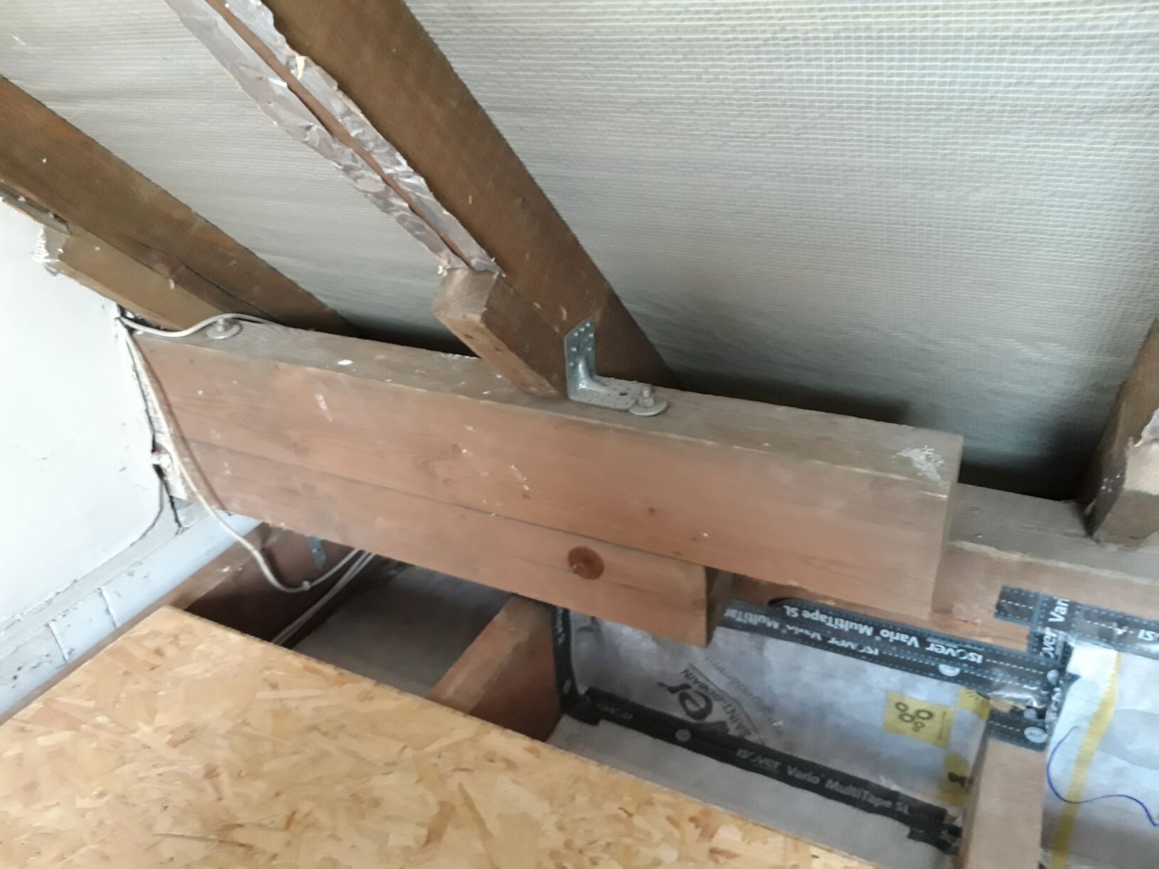 Dachboden: Holzbalken, Metallwinkel, Dämmung und Kabel am OSB-Boden.